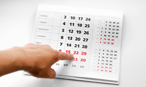 finger pointing to a calendar with some dates in red